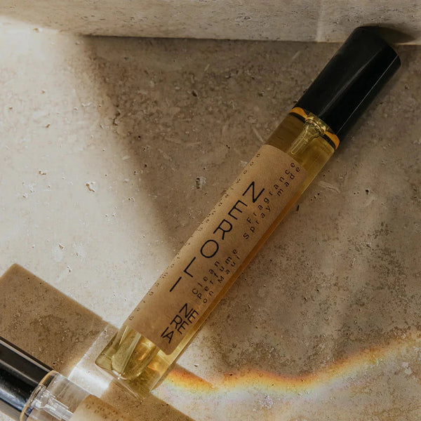 Two small perfume bottles with visible branding on a textured surface with a rainbow effect.