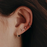 Close-up of an ear wearing two small hoop earrings with a dark background